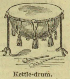 A kettle drum with tassels hanging from its rim stands on three legs, with two drumsticks lying in front.
