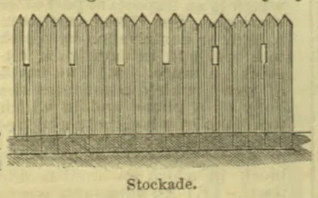 A wooden stockade fence made of pointed vertical stakes.
