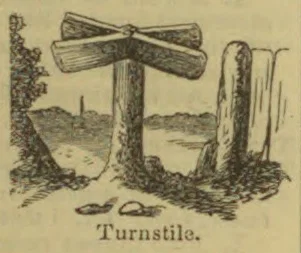 A wooden turnstile barrier stands beside a path in a rural landscape.
