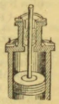 A cutaway view of a vertical mechanical device with a central rod, a cylindrical lower chamber, and a sturdy frame.